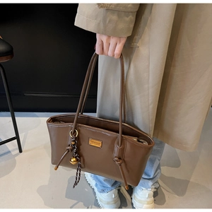 Detail of dark brown oil wax leather tote bag with gold plaque and metal ball charm