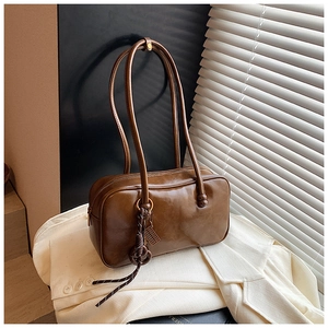 Détail d'un sac Boston en cuir ciré marron avec breloques tressées et ombres lumineuses