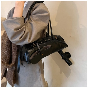Detail of black glossy faux leather baguette bag with metal eyelet strap on model