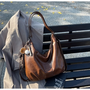 Borsa hobo marrone vintage con ciondoli da baseball su una panchina tra foglie autunnali
