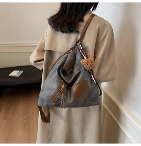Detail view of large grey hobo bag with brown leather trim and cute bear charm