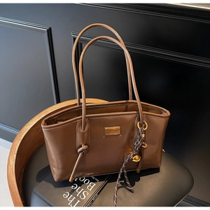 Close-up of brown oiled leather tote bag with gold logo plate and woven knot charm detail