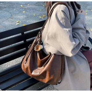 Dettaglio di borsa hobo in pelle marrone vintage con ciondoli da baseball e texture