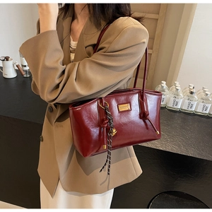 Close-up of wine red oil wax leather tote bag with elegant metallic charm on shoulder strap