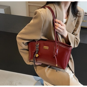 Detail of burgundy oil wax leather tote bag with gold nameplate and decorative pendant