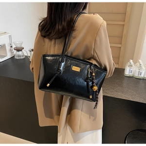 Detailed close-up of a black patent leather shoulder bag with a gold metal logo plate