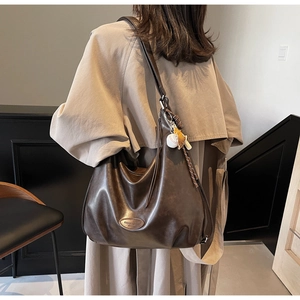 Dettaglio della grande borsa tote in pelle marrone scuro con ciondoli su un trench coat