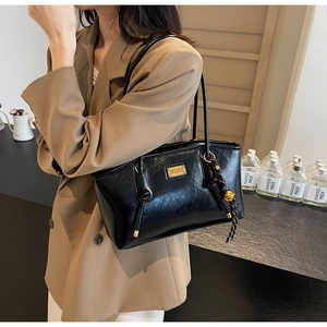 Detail of black wax leather tote with fashion metal plate and braided bell pendant