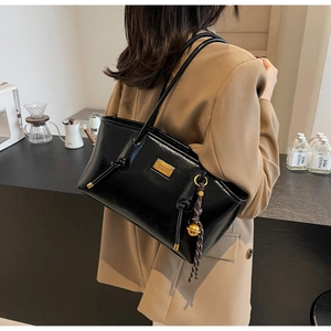 Detailed side view of black glossy leather shoulder bag with gold bell charm on model