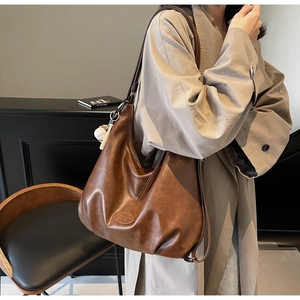 Dettaglio della borsa tote in pelle marrone con logo a rilievo e ciondolo da baseball