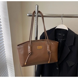 Detail of dark brown leather tote featuring a unique knotted handle and gold metal plate