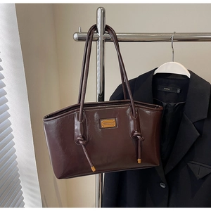 Detail of dark brown glossy leather tote bag with elegant gold metal knots and brand plaque