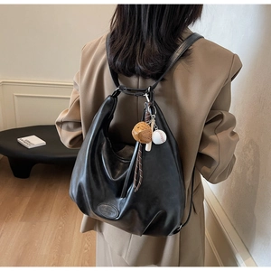 Dettaglio borsa hobo nera con ciondolo da baseball e logo moda su pelle morbida e lucida