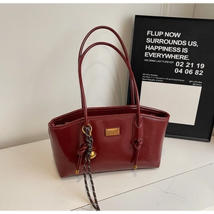 Detail of burgundy wax leather handbag with gold metal logo and braided rope pendant
