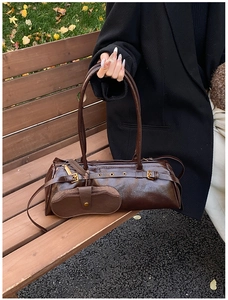 Detailed view of dark brown oil wax leather baguette bag with gold metal hardware on bench