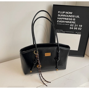 Detail of glossy black oil wax leather tote bag with gold logo plate and tassel
