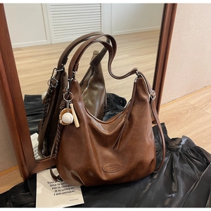 Dettaglio della borsa hobo in pelle marrone vintage con logo e ciondolo a tema baseball
