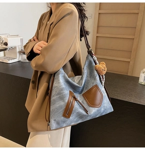 Detail of blue textured hobo bag with brown leather trim and hanging bear charm accessory