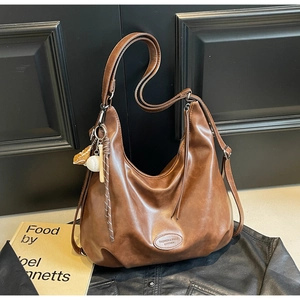 Dettaglio della borsa Hobo vintage marrone con ciondolo da baseball e tracolla larga
