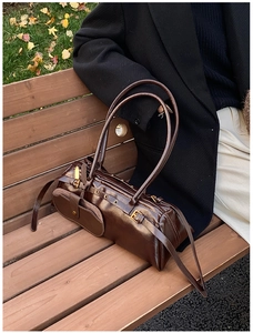 Detail of dark brown oil-wax leather baguette bag with metal buckles on park bench