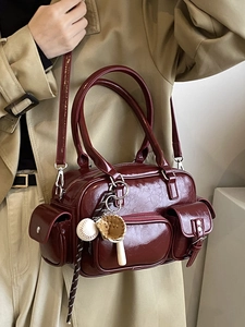 Minimalist burgundy bowling bag with multiple pockets and sports charm on trench coat