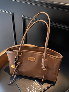 Brown oil-wax leather bucket bag with metal logo and woven knot pendant on a vintage chair