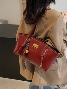 Elegant wine red glossy leather tote bag featuring a gold nameplate and knotted strap