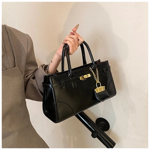 Detail of black patent leather briefcase with gold twist lock and mini bag charm accessory