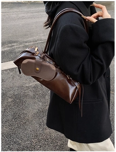 Side view of a dark brown oiled leather baguette shoulder bag worn over a black coat