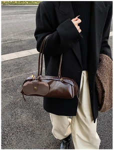 Detailed street shot of a vintage dark brown cylindrical shoulder bag with glossy leather texture