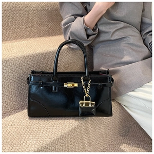 Detail of black glossy leather briefcase with gold hardware and mini bag charm accessory