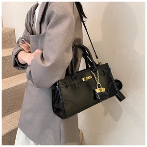 Detail einer schwarzen glänzenden Handtasche mit goldenem Drehschloss und Anhänger