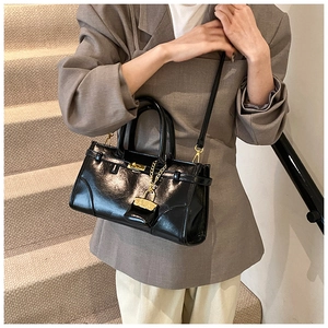 Chic black patent leather handbag with gold twist lock and mini charm shown on model