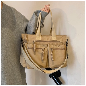 Close-up of khaki tote bag featuring three front zipper pockets and braided cord pulls