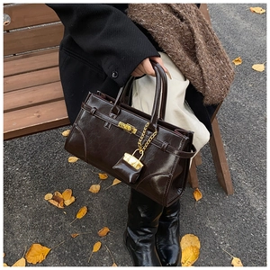 Detail of a dark brown glossy vintage briefcase bag with golden lock on park bench