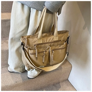 Detail view of khaki nylon tote bag featuring front zipper pockets and woven zip pulls