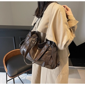 Détail du sac fourre-tout marron foncé avec œillets argentés et brides sur un manteau beige