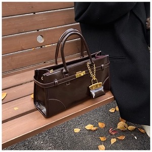 Detail einer dunkelbraunen Lackledertasche mit goldenem Drehverschluss und Anhänger