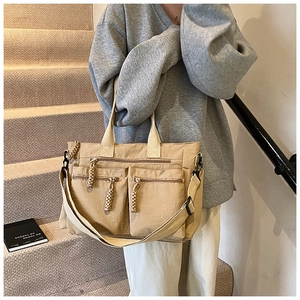 Close-up of khaki canvas tote bag featuring dual front zipper pockets and braided pulls