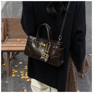 Dark brown patent leather briefcase with gold hardware shown on a park bench