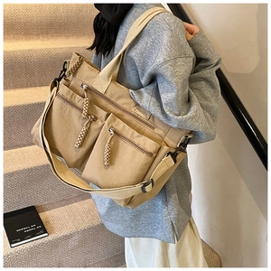 Close-up of khaki canvas tote bag featuring double front zipper pockets and woven pullers