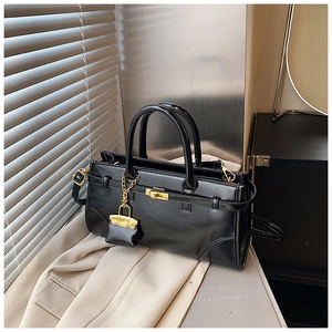 Detail of black glossy leather briefcase featuring gold hardware and a mini bag charm