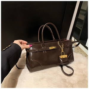 Detail of dark brown glossy leather handbag with golden metal twist lock and micro charm