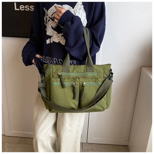 Detail of green canvas tote bag showing multiple functional zipper pockets and woven pullers
