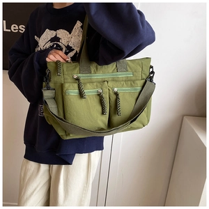Detail of army green nylon tote bag featuring multiple functional zipper pockets and straps