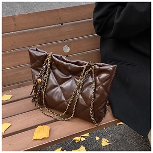 Detail of dark brown quilted tote bag with chain strap on autumn leaves bench
