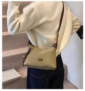 Detalle de bolso bandolera verde oliva con placa metálica y colgante trenzado