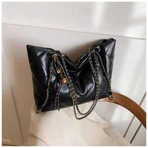 Close-up of black quilted tote bag with golden chain strap and tassel on a suit chair