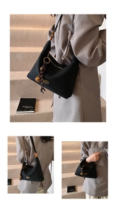Detalle de un bolso de axila negro con borla dorada en una modelo con estilo actual