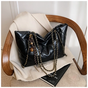 Detailed close-up of the black quilted tote bag with gold chain strap on a vintage chair